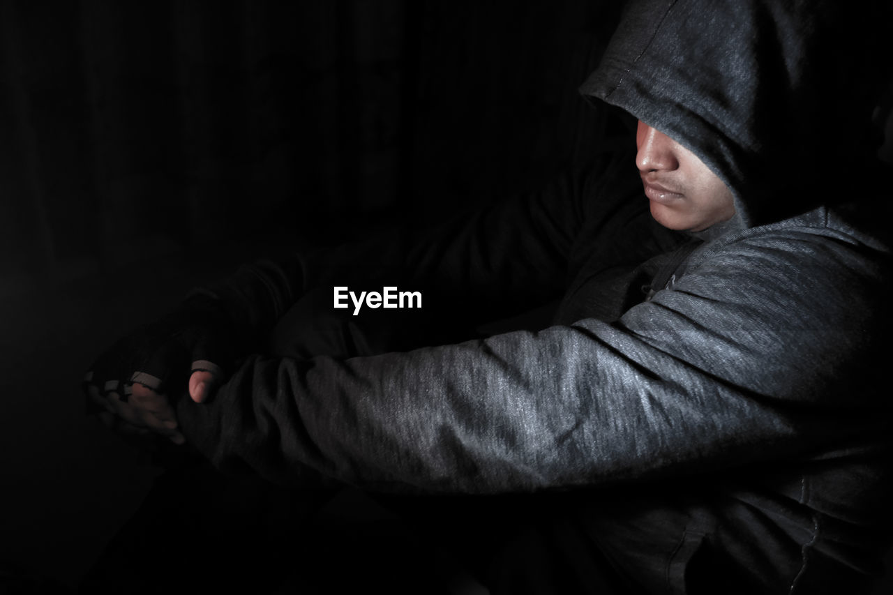 Hooded depressed man sitting on floor in dark room.