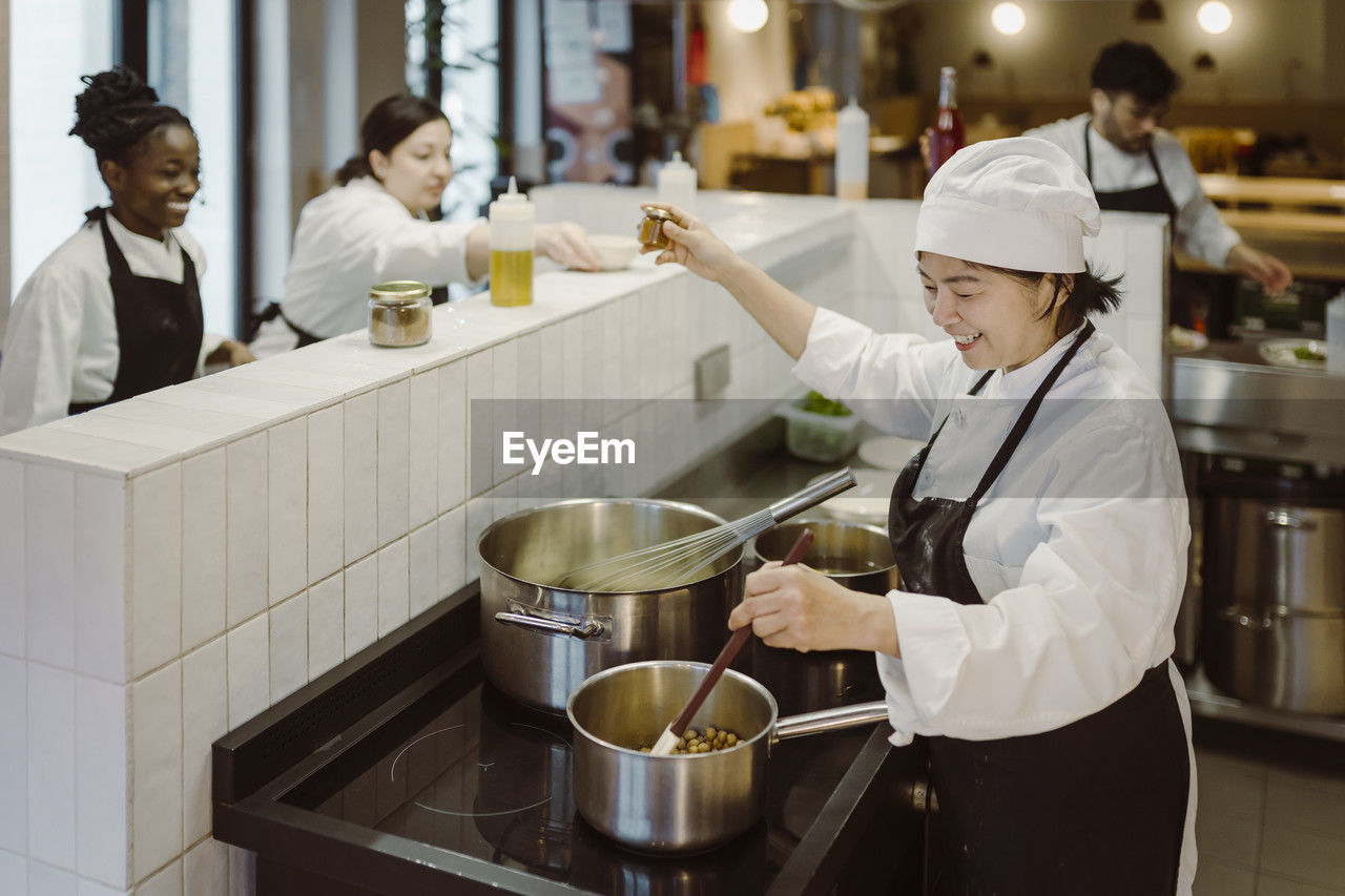 High angle view of female chef multi-tasking while standing with colleagues in commercial kitchen