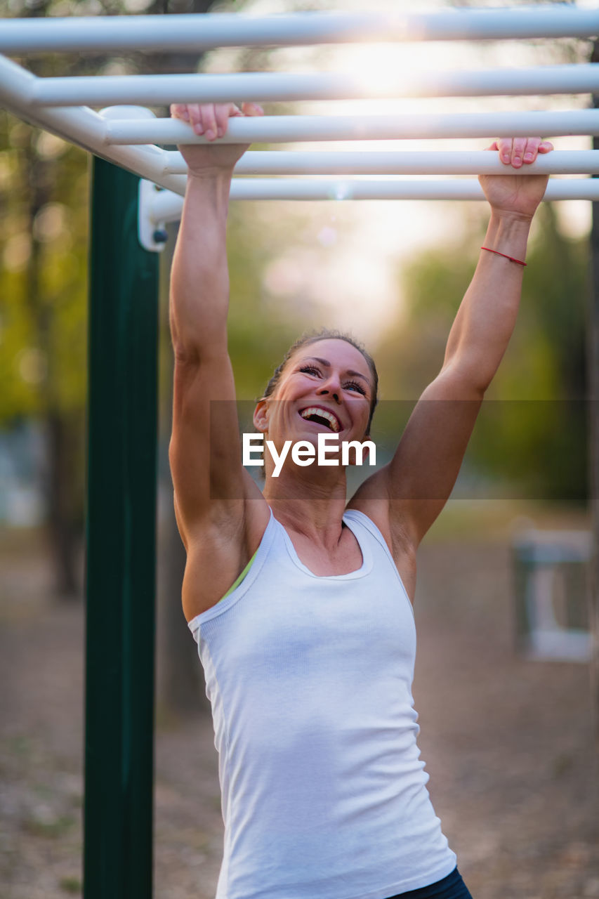 Smiling woman hanging on monkey bars in park