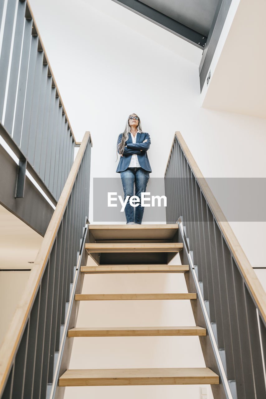 Confident businesswoman with long grey hair standing on top of stairs