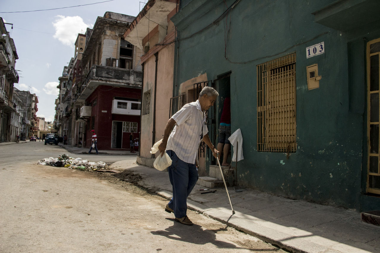 FULL LENGTH REAR VIEW OF MAN WALKING ON STREET AGAINST BUILDINGS