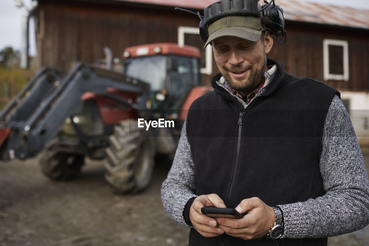 Farmer with cell phone standing next to tractor