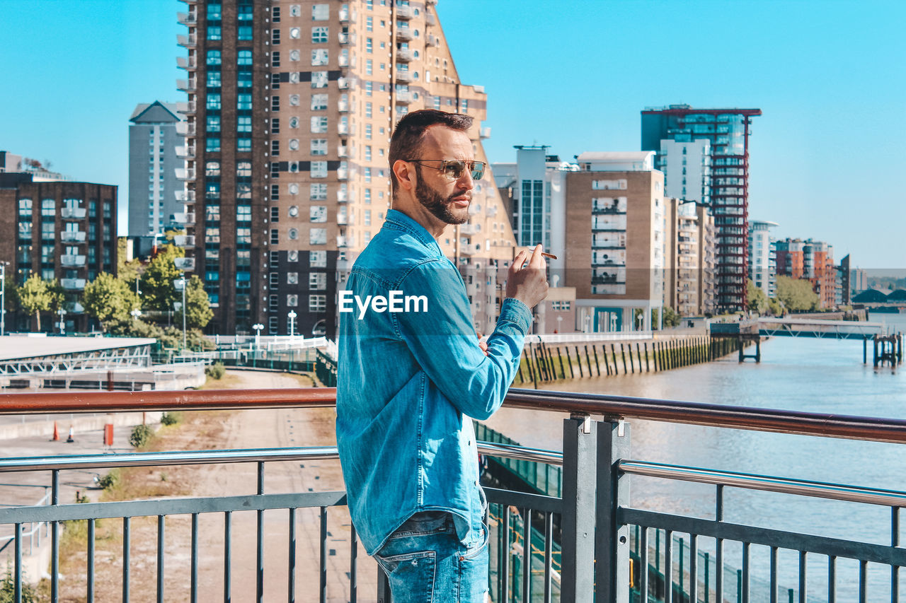 Side view of man standing by railing against buildings in city