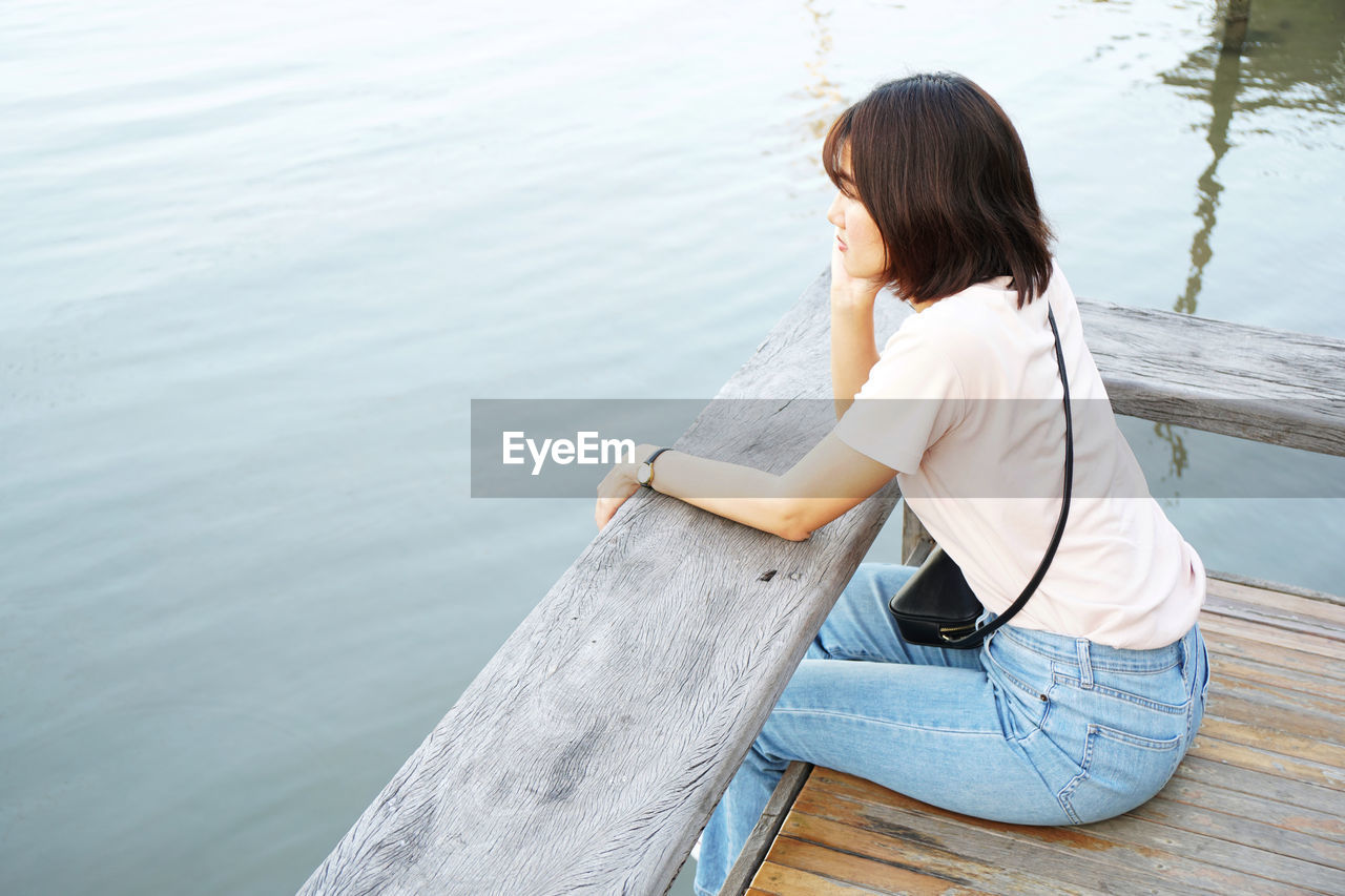 Woman sitting on pier by lake