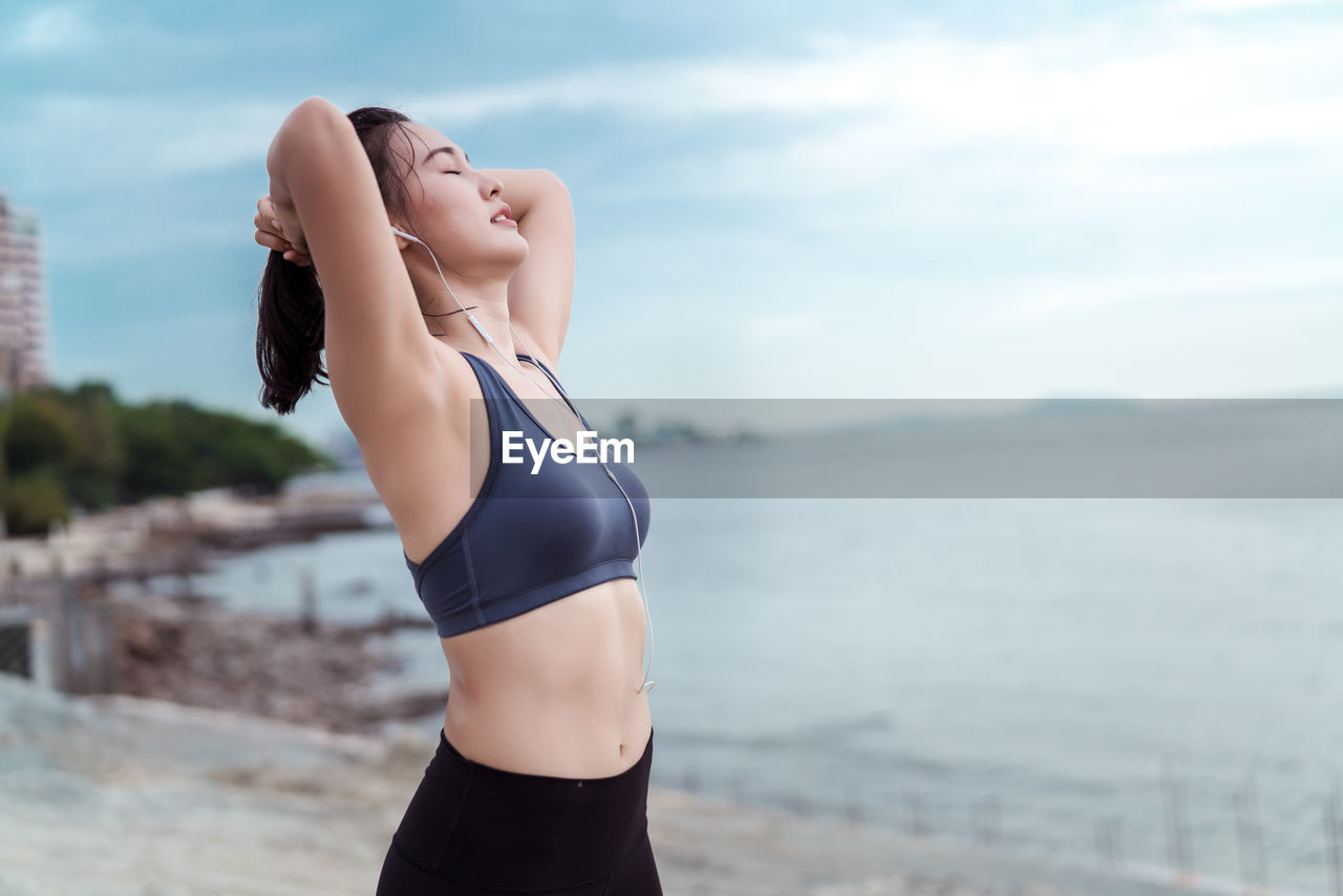 Young woman exercising at beach against sky