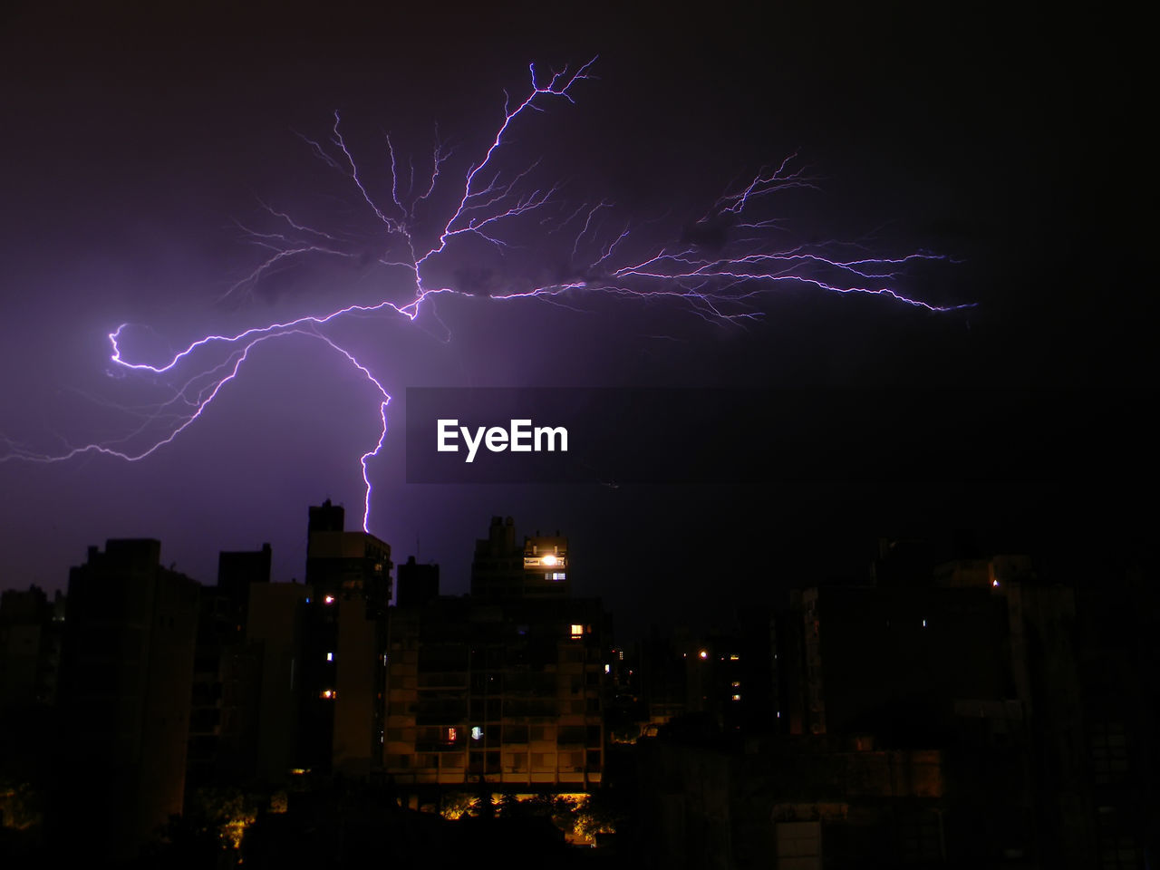 Lightning over buildings against sky at night