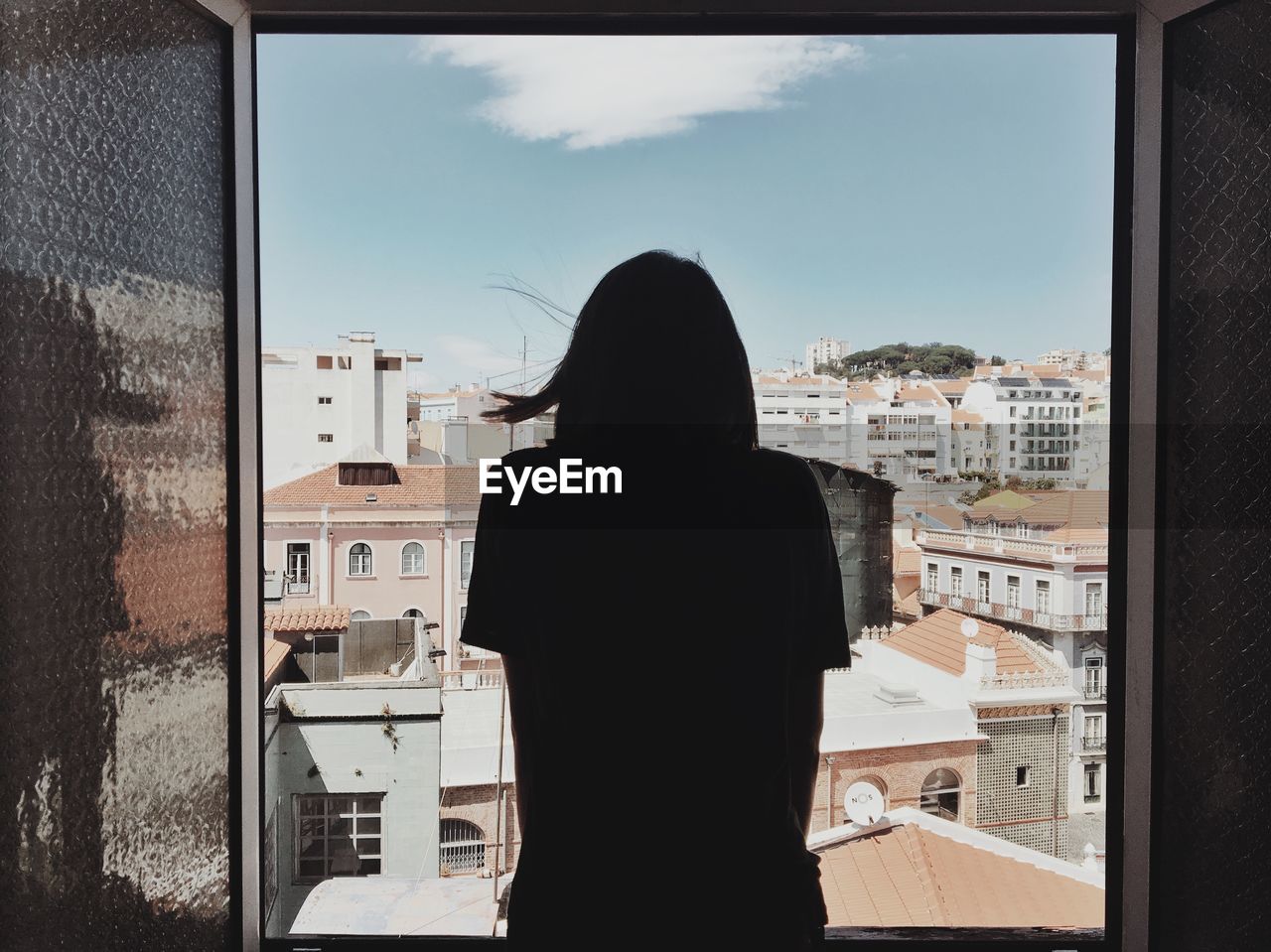 Rear view of woman looking through window by buildings against sky