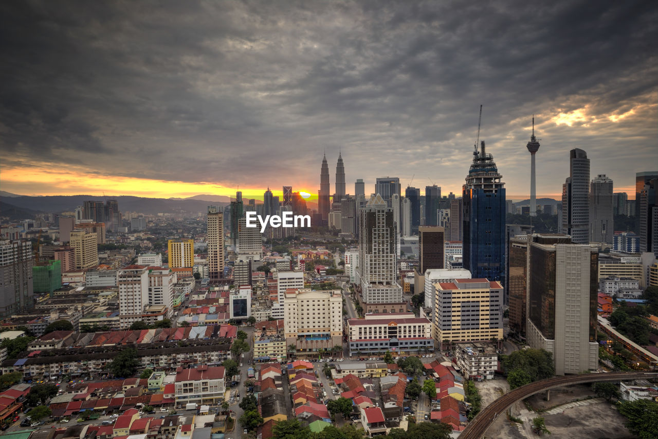 Distant view of petronas tower against cloudy sky during sunset in city