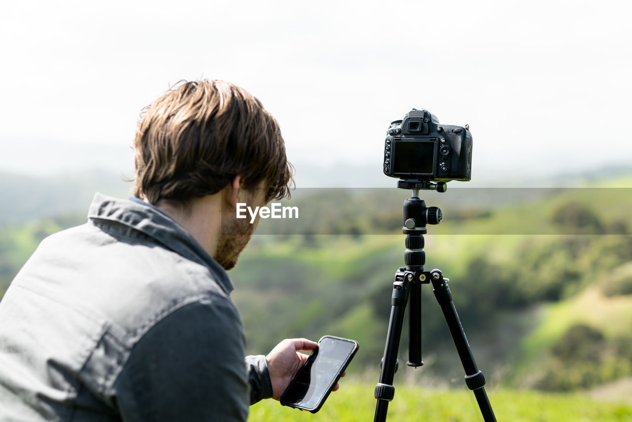 Person using smartphone app to control camera on tripod outdoors