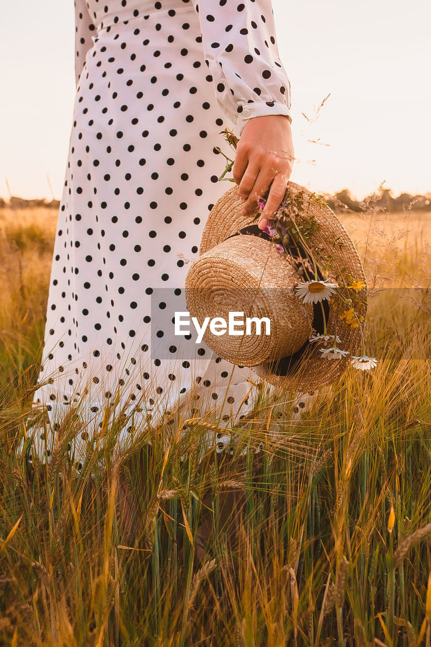 MIDSECTION OF WOMAN HOLDING BASKET IN FIELD