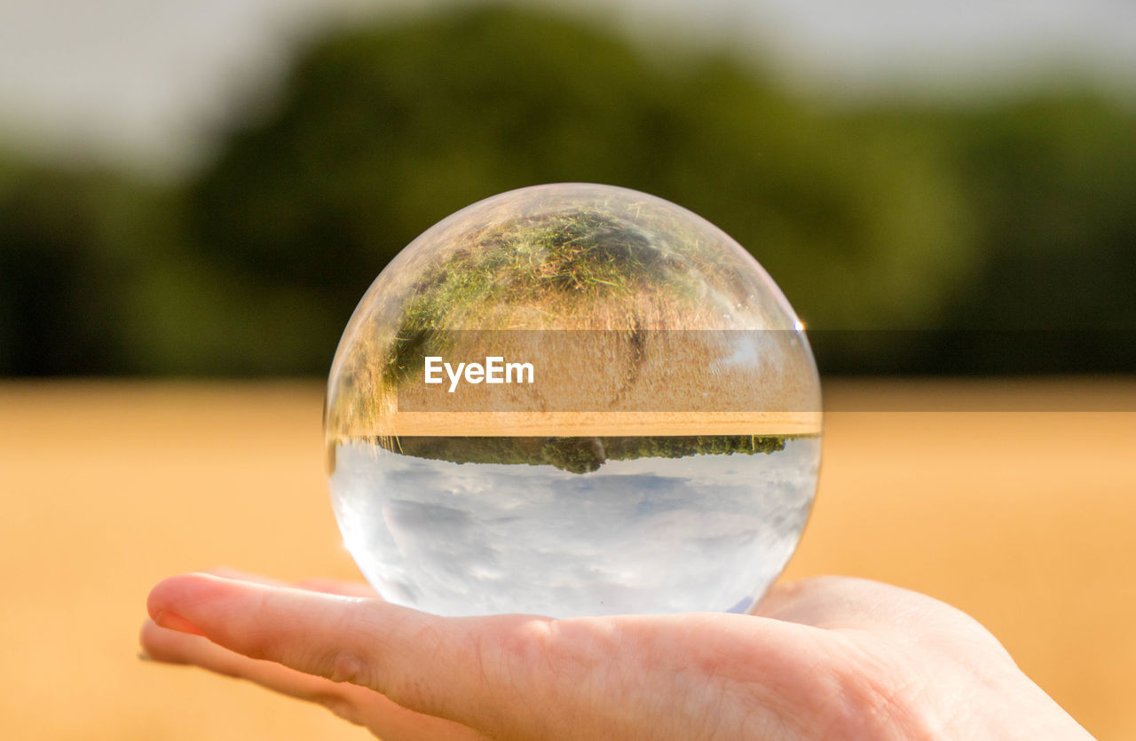 CLOSE-UP OF HAND HOLDING CRYSTAL BALL WITH WATER DROPS