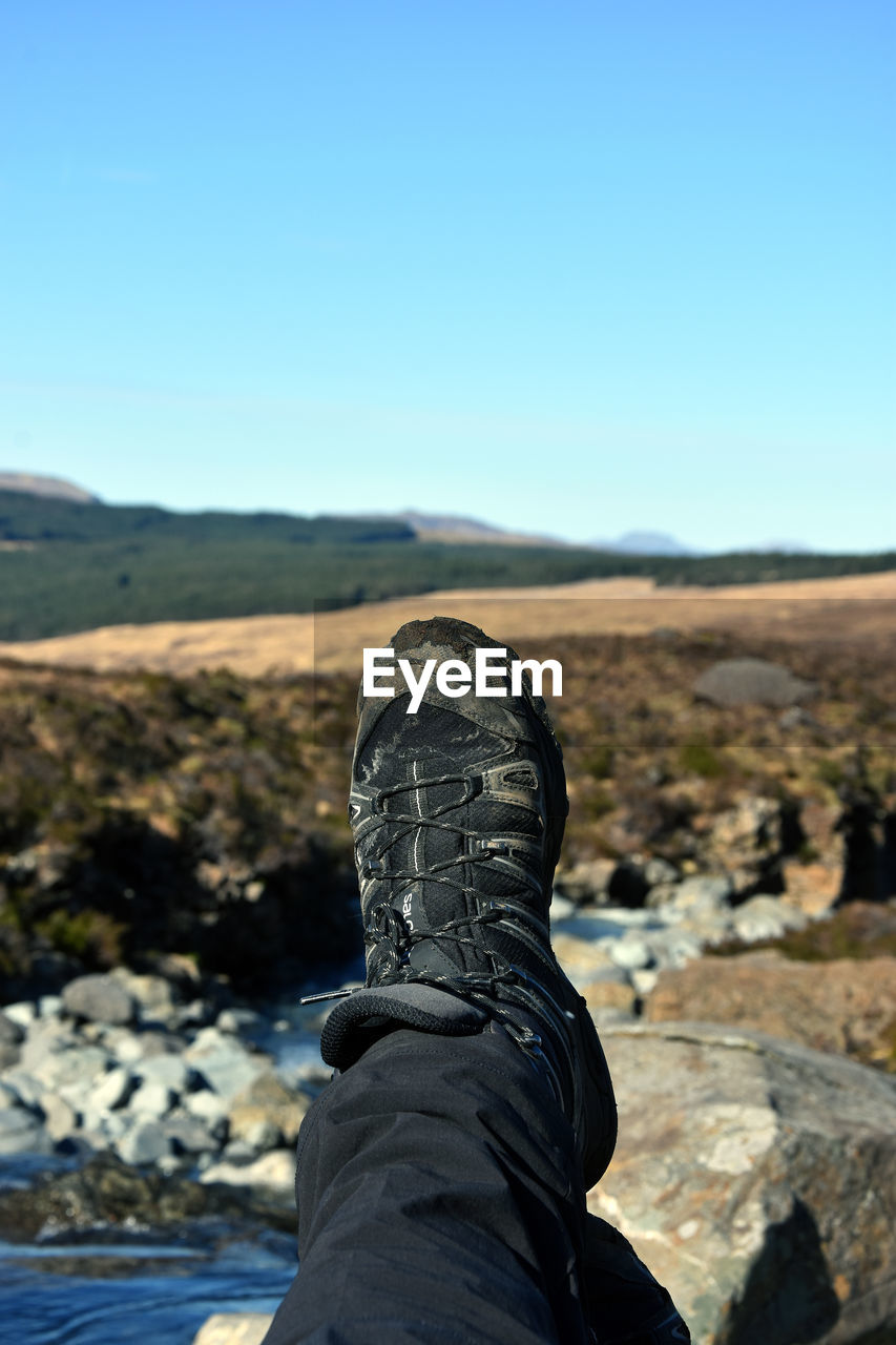 Cropped image of person with feet up on mountain against clear sky