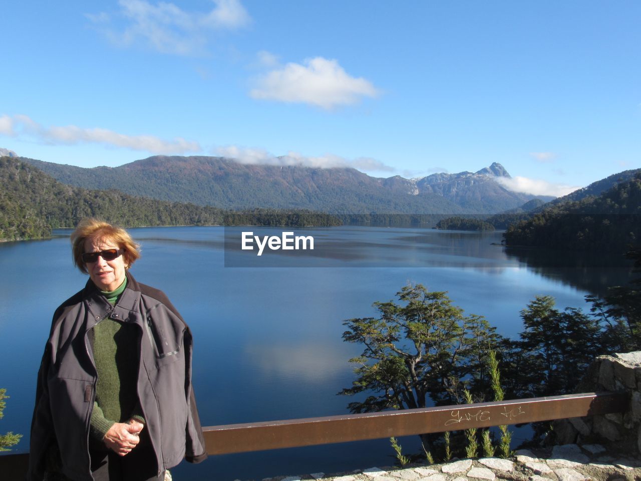 Portrait of senior woman wearing sunglasses while standing against lake