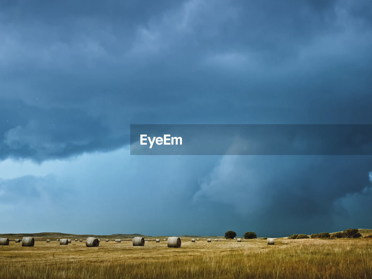 Hay bales on field against cloudy sky