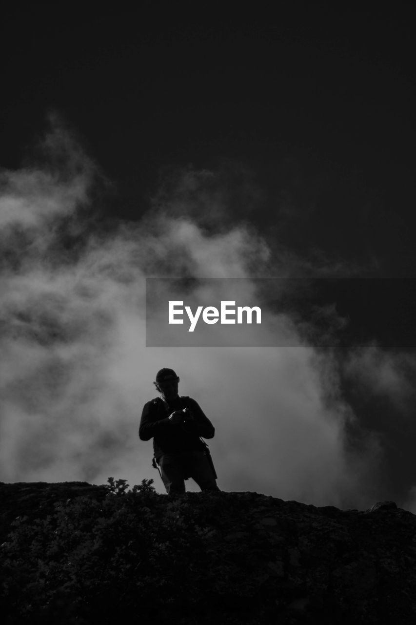 Low angle view of silhouette man standing on rock against sky