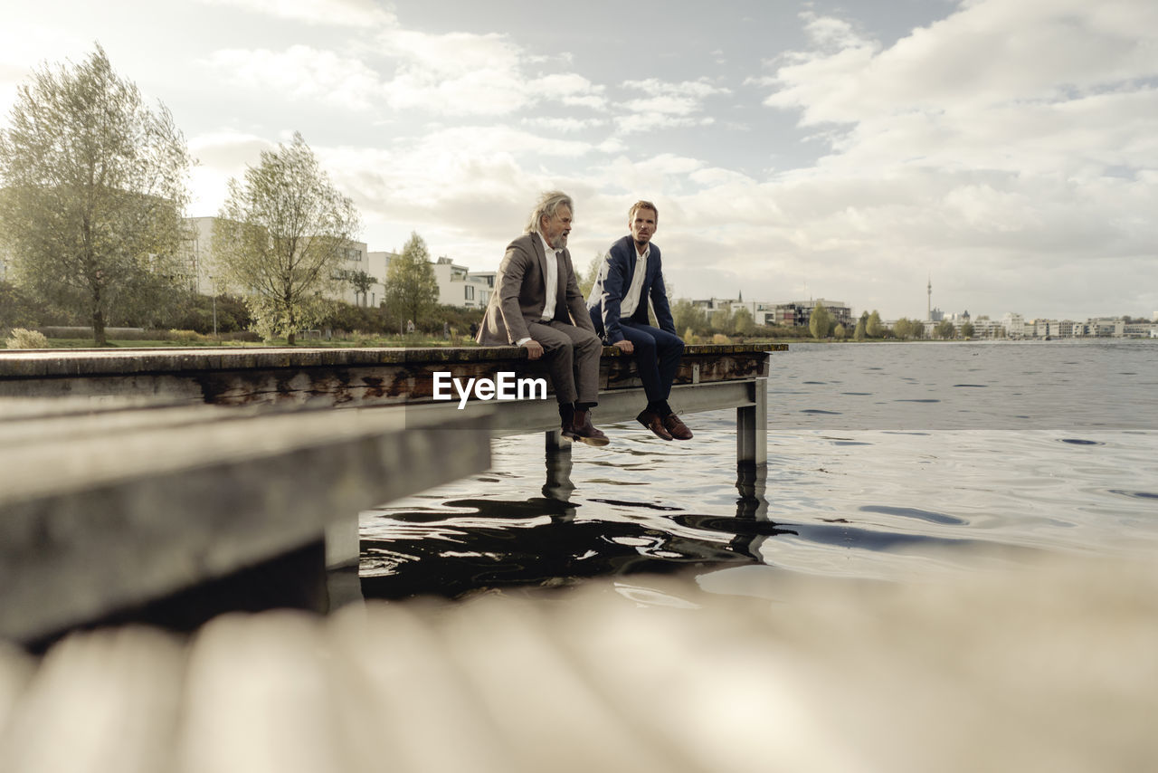 Two businessmen sitting on jetty at a lake