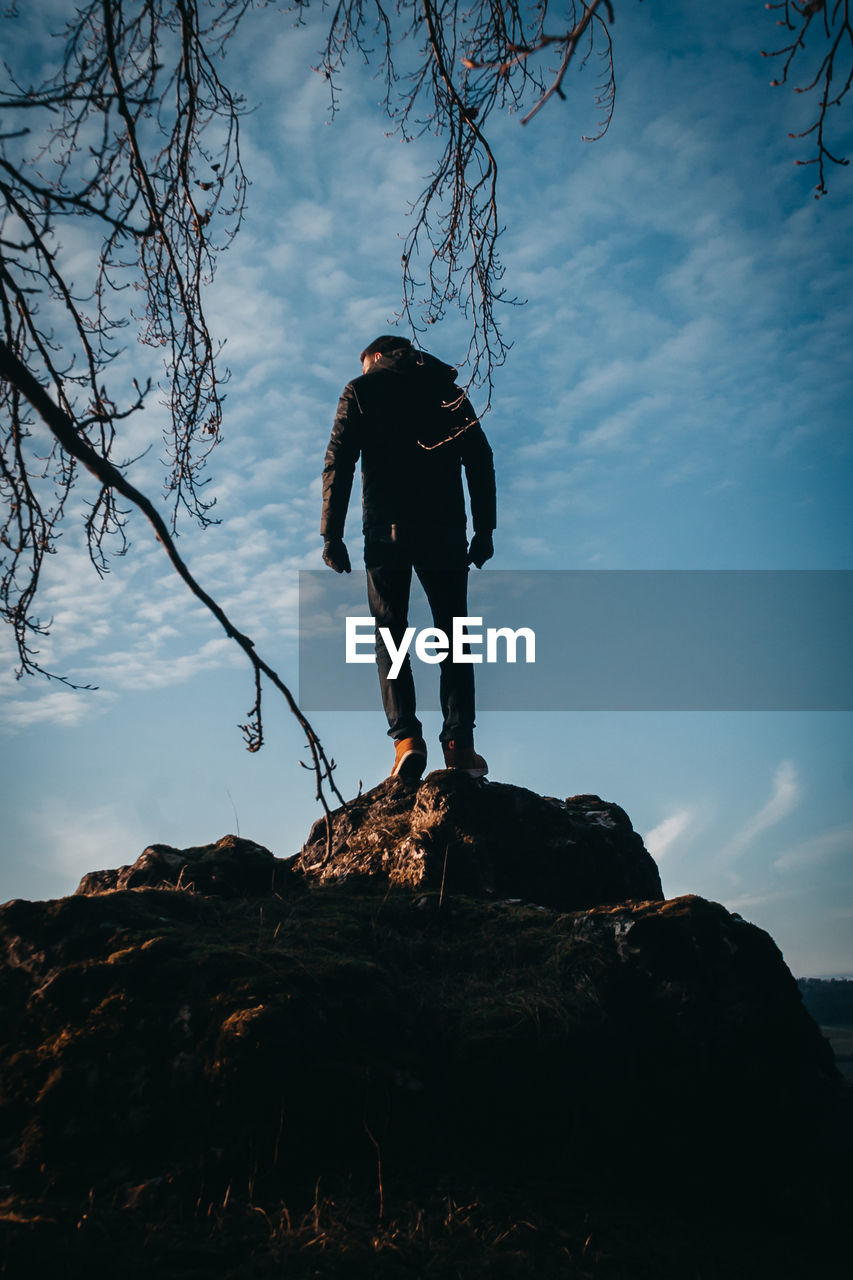 LOW ANGLE VIEW OF MAN STANDING ON ROCK