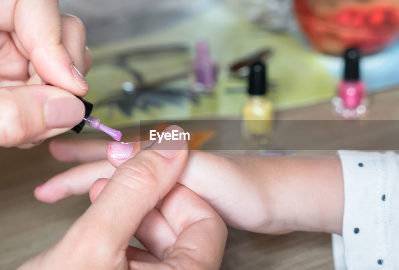 Cropped hands applying nail polish on girl fingernail