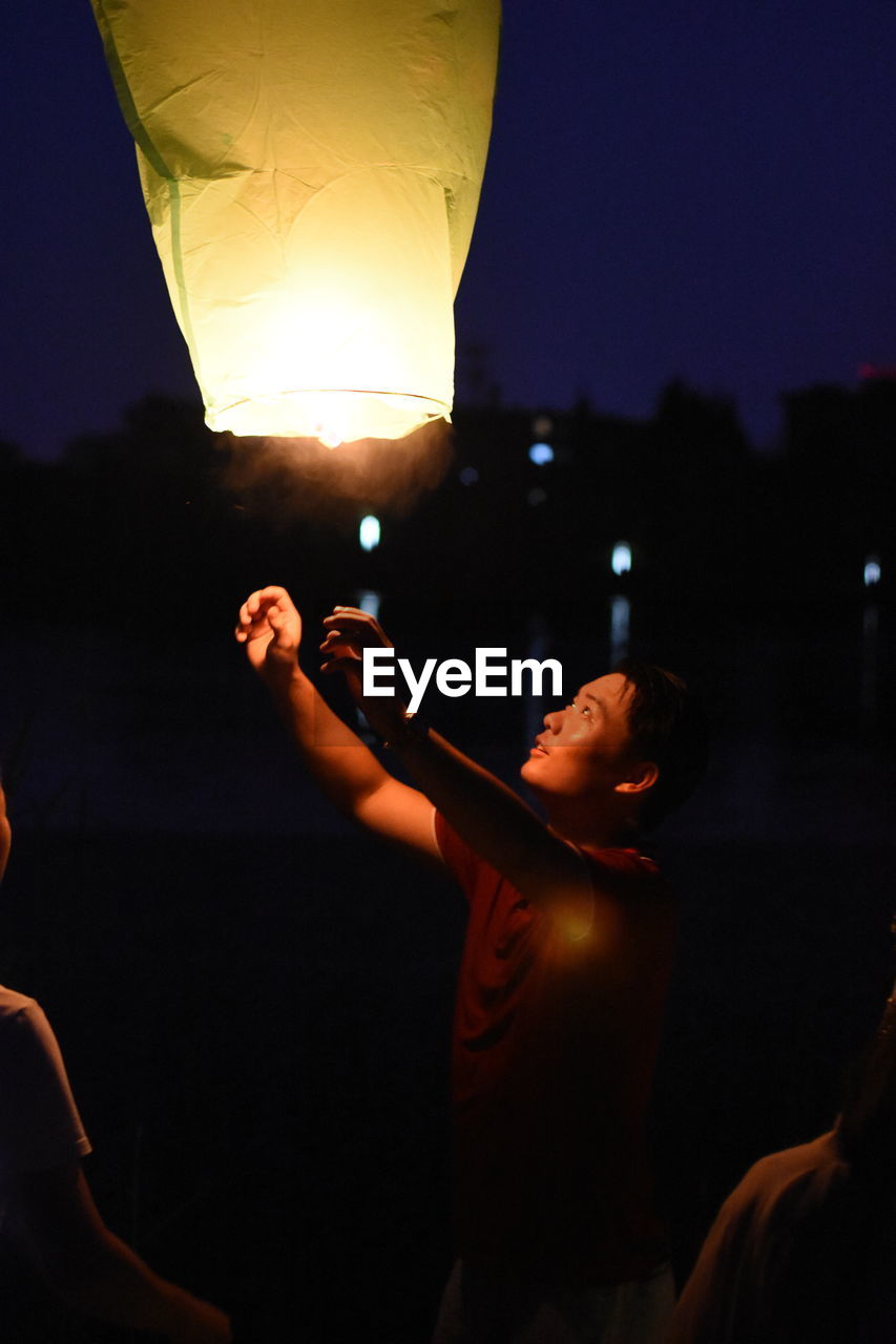 CLOSE-UP OF HAND HOLDING ILLUMINATED LIGHTING EQUIPMENT AT NIGHT