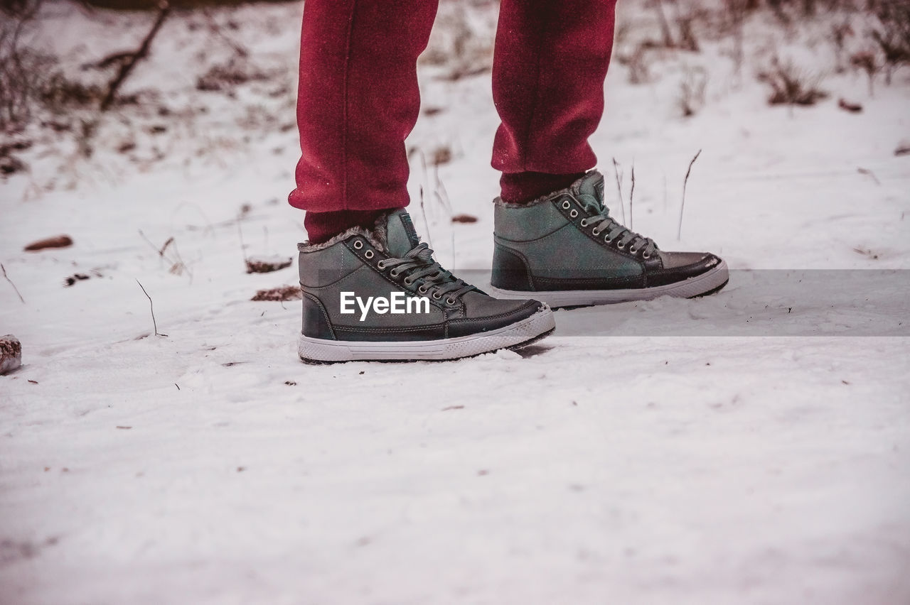 low section, human leg, red, shoe, winter, footwear, snow, white, human limb, limb, one person, cold temperature, spring, standing, day, nature, lifestyles, black, leisure activity, outdoors, land, winter sports, adult, clothing, human foot, selective focus, men, sports, pink