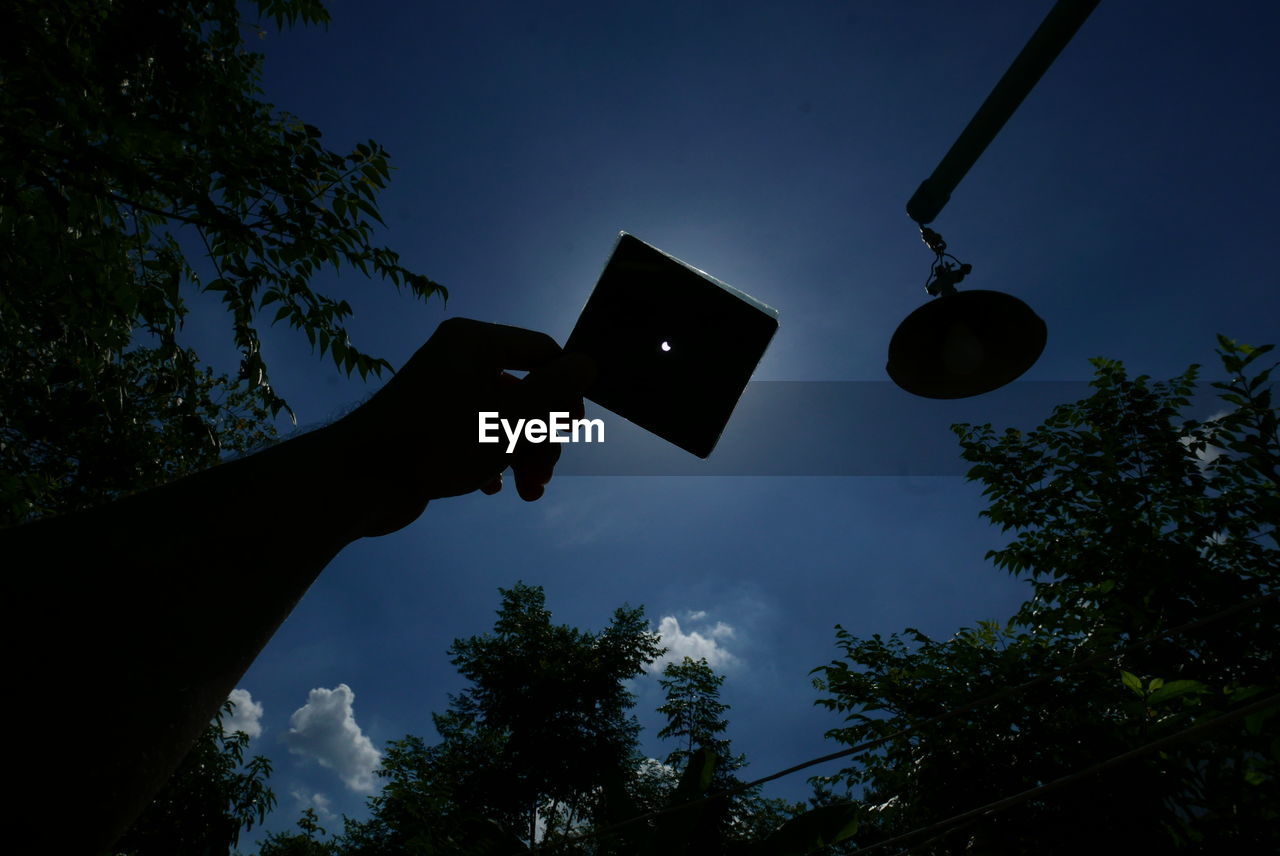 LOW ANGLE VIEW OF PERSON HAND HOLDING MOBILE PHONE AGAINST SKY