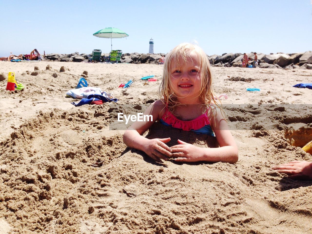 Cute smiling girl buried in sand at beach during summer