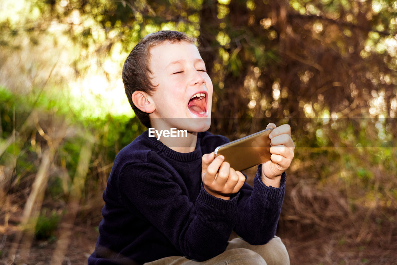 Boy holding mobile phone while sitting outdoors