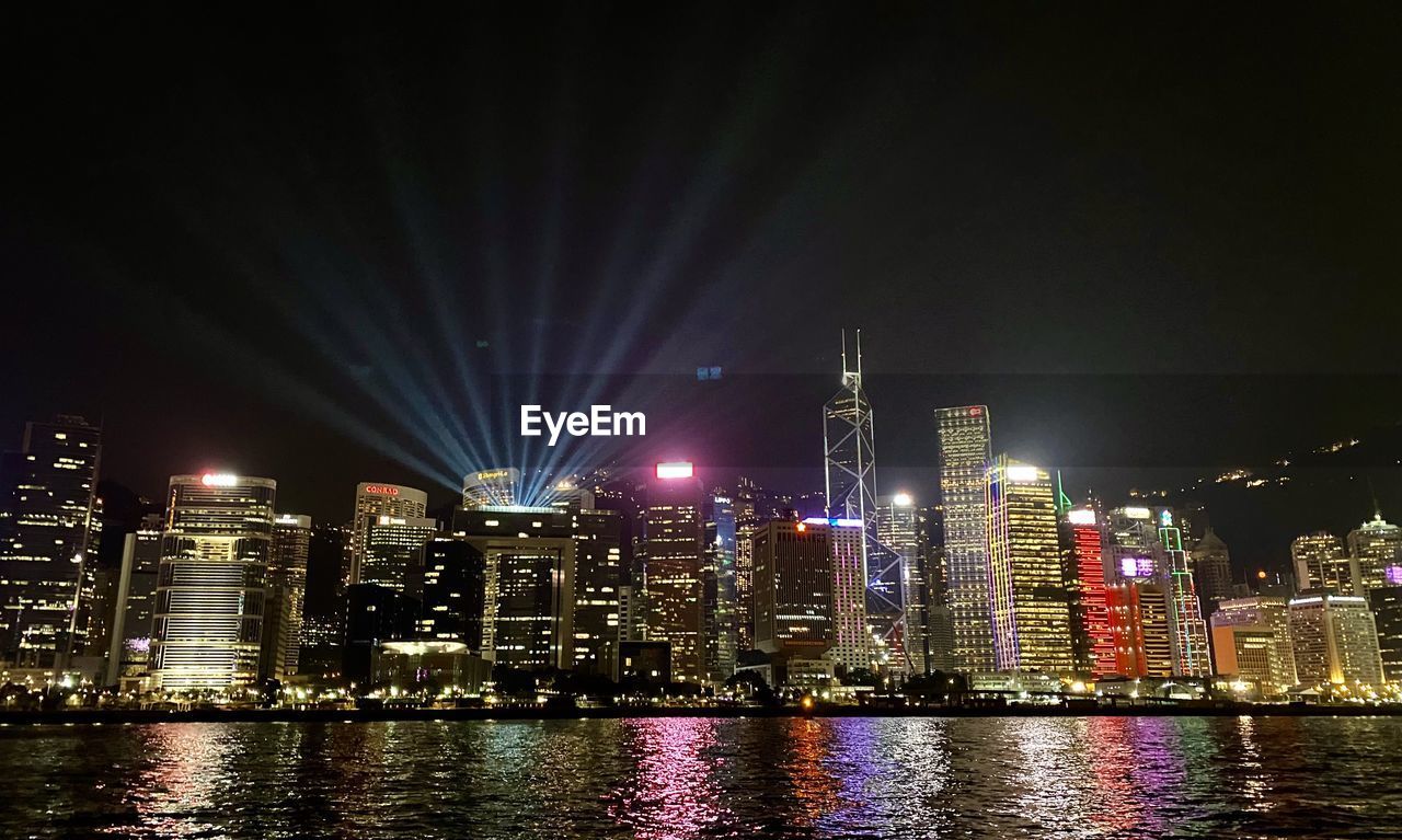 ILLUMINATED BUILDINGS BY RIVER AGAINST SKY