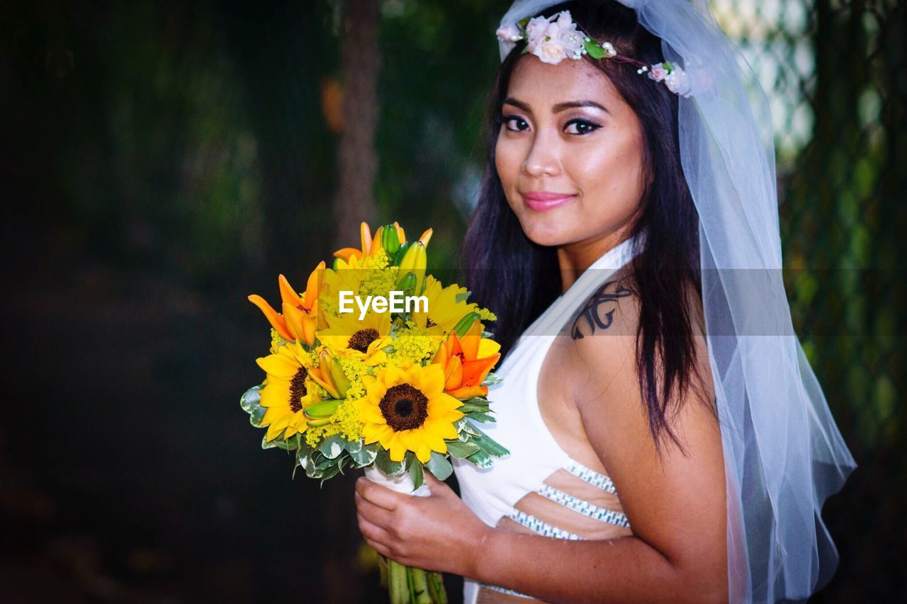 Portrait of smiling bride holding bouquet standing outdoors