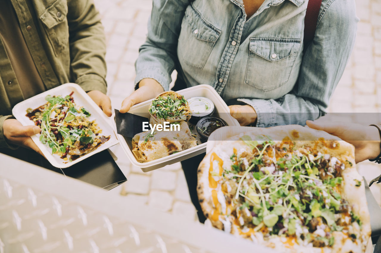 Midsection of customers holding indian street food in city