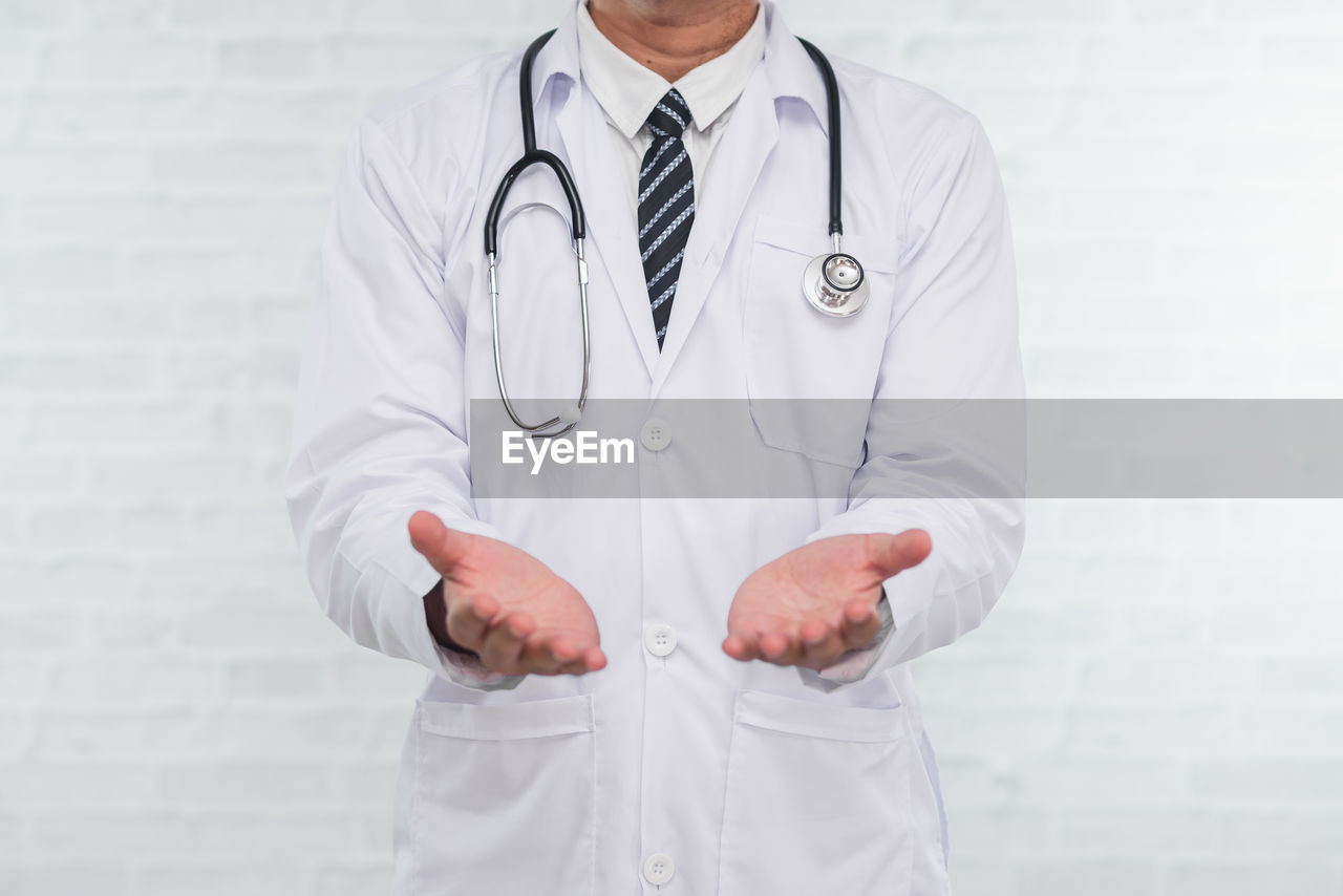 Midsection of doctor gesturing while standing against wall