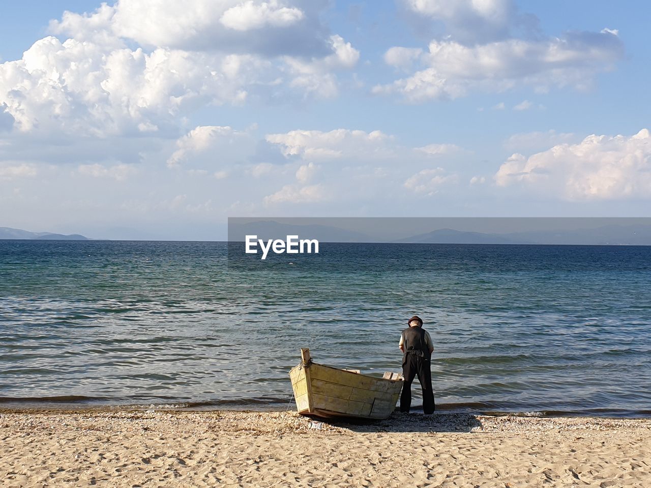 Rear view of man standing by moored boat at beach against sky