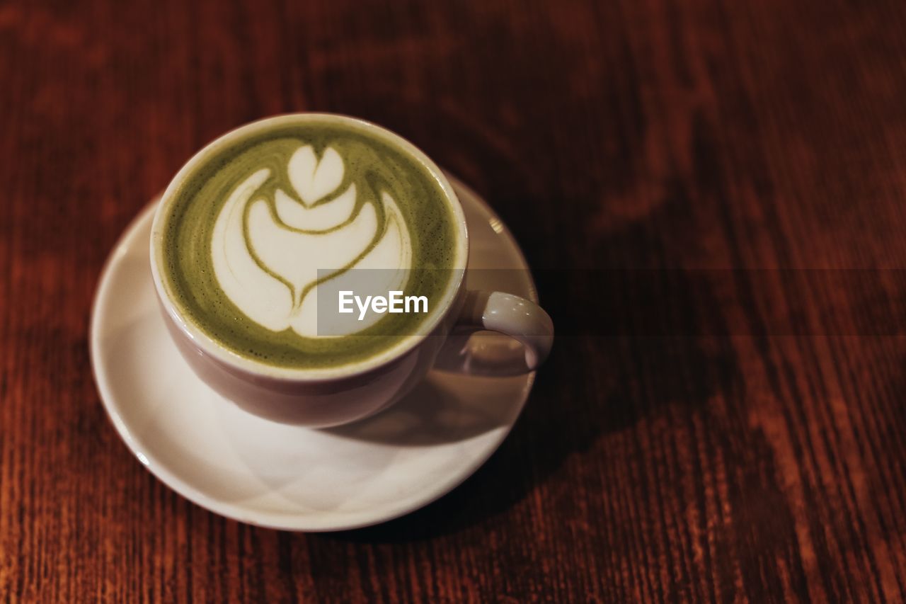 A cup with organic green japanese matcha tea and milk foam on a wooden table.