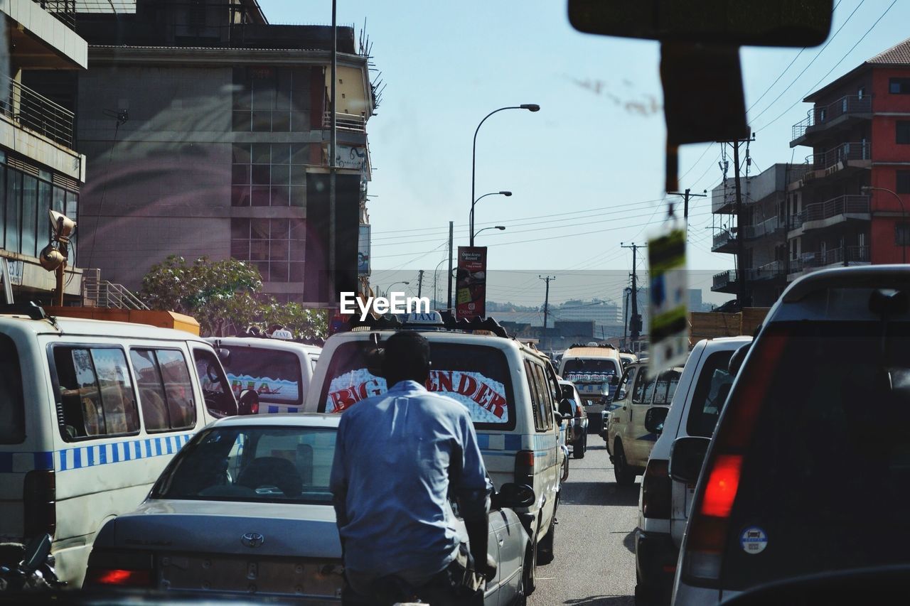 REAR VIEW OF VEHICLES ON ROAD ALONG BUILDINGS