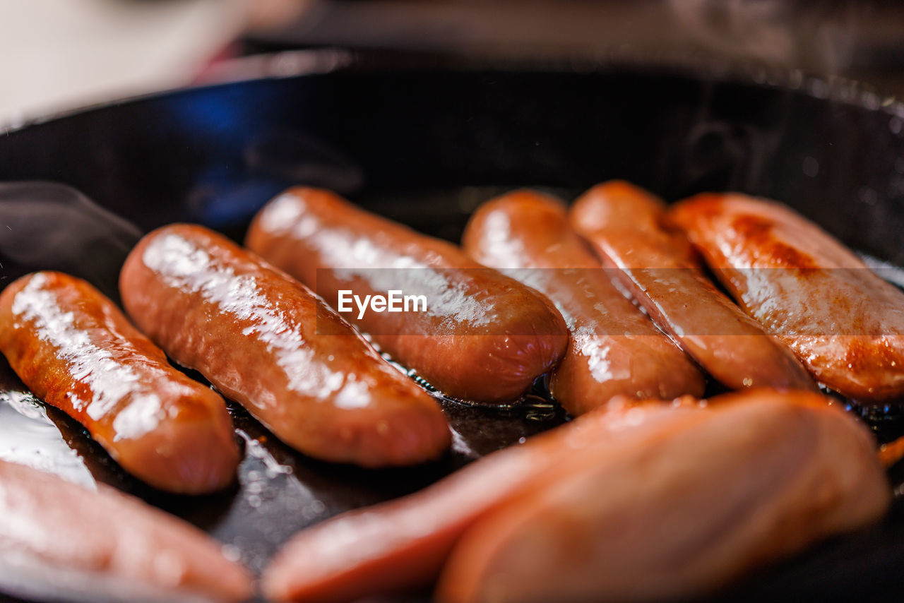 Half-cut sausages are fried in oil in a black cast iron skillet