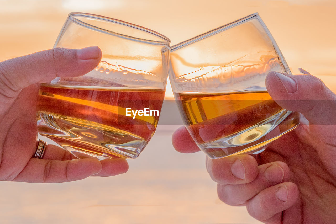 Cropped image of hands toasting against sea