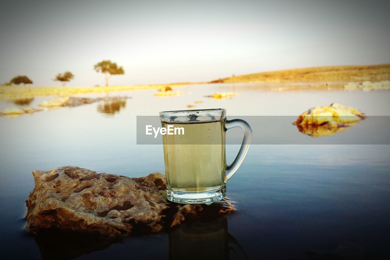 Drink in glass on rock against lake