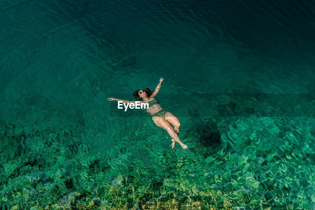 Aerial of woman floating on back in crystal clear water relaxing on vacation.