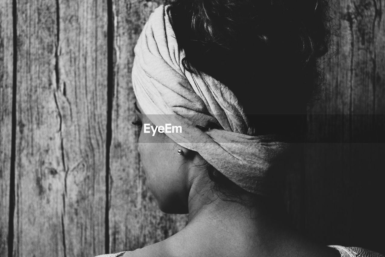 Rear view of woman wearing headdress against wooden wall