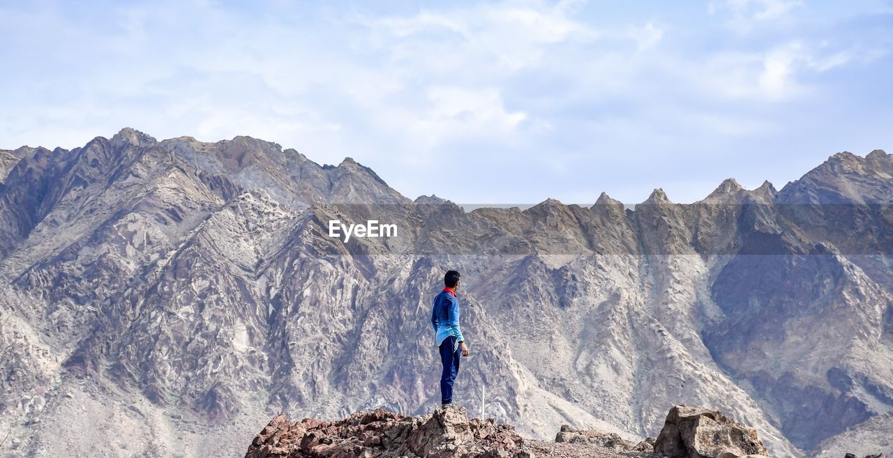 Boy standing on rock against mountains and sky