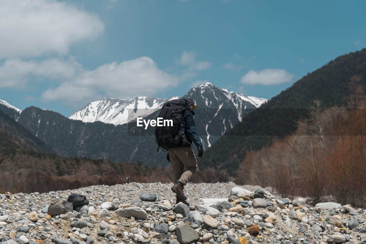 Side view of backpacker walking on land with mountains in background