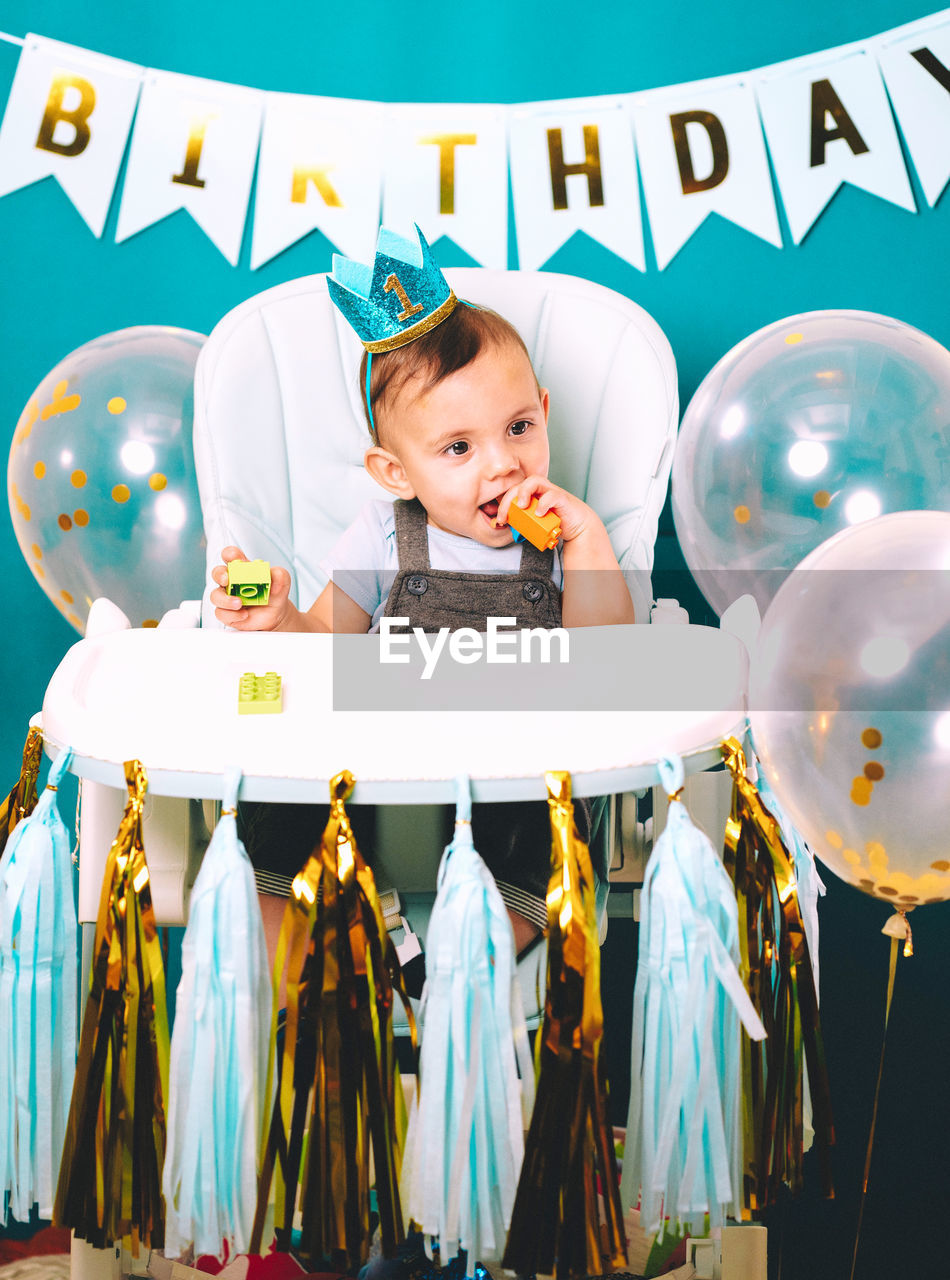 Cute baby boy sitting on high chair in birthday party