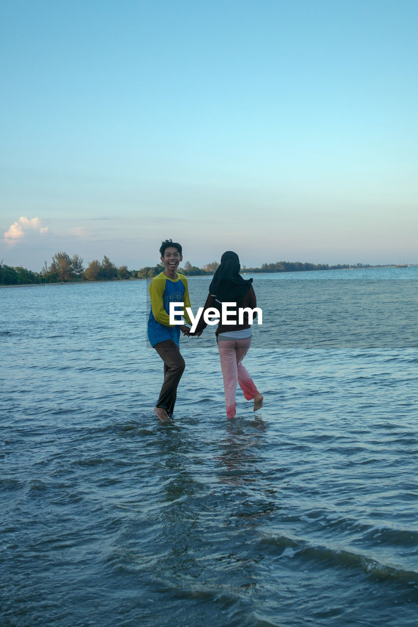 Couple standing in sea against sky