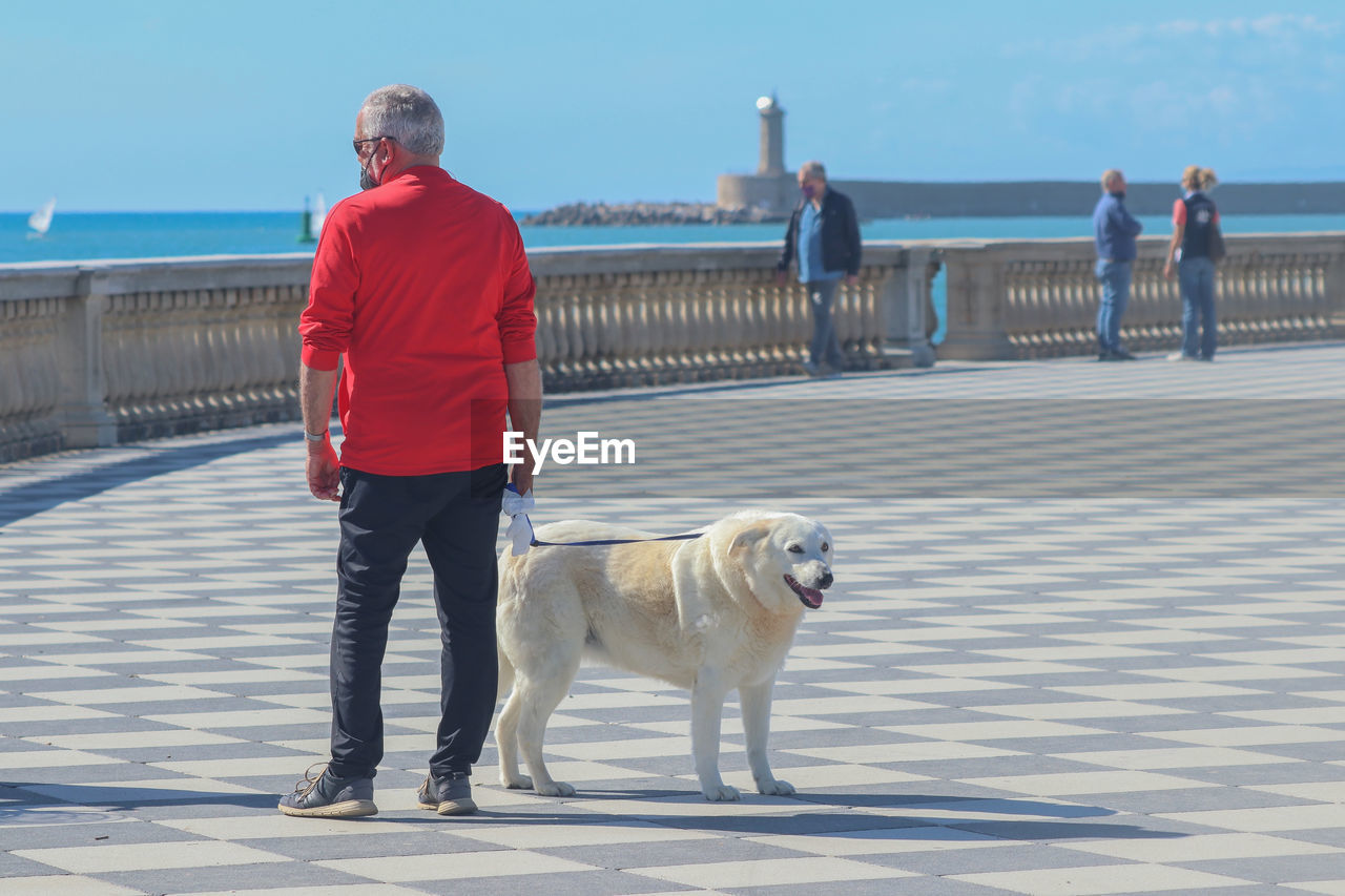 Mature man with dog on shore against sky at mascagni terrace.