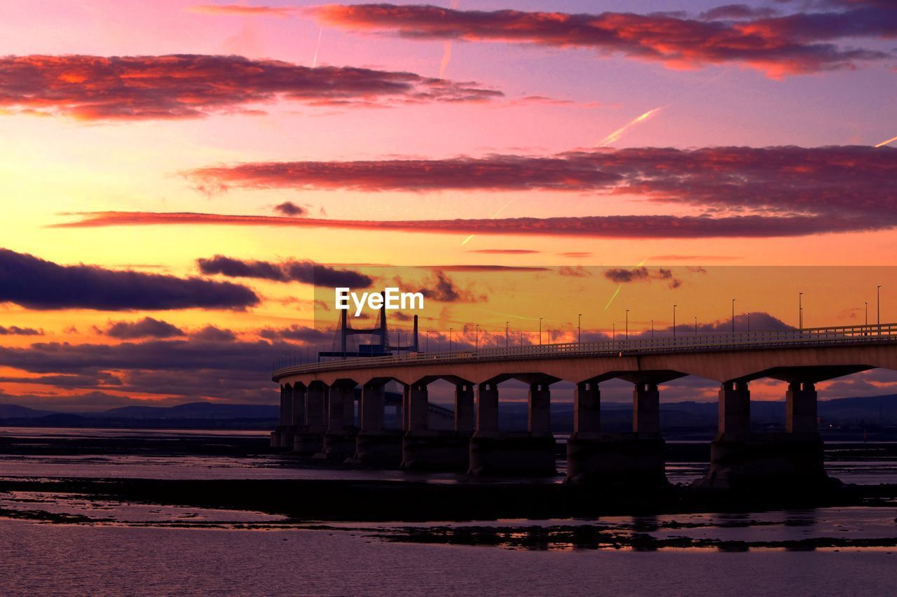 Silhouette bridge over sea against romantic sky at sunset