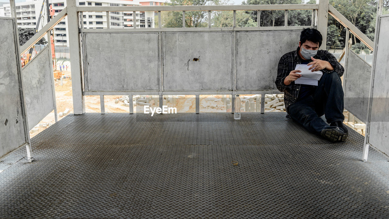 FULL LENGTH OF YOUNG MAN SITTING ON MOBILE PHONE WHILE STANDING ON WALL