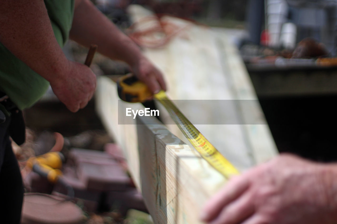 Midsection of carpenter measuring wooden plank