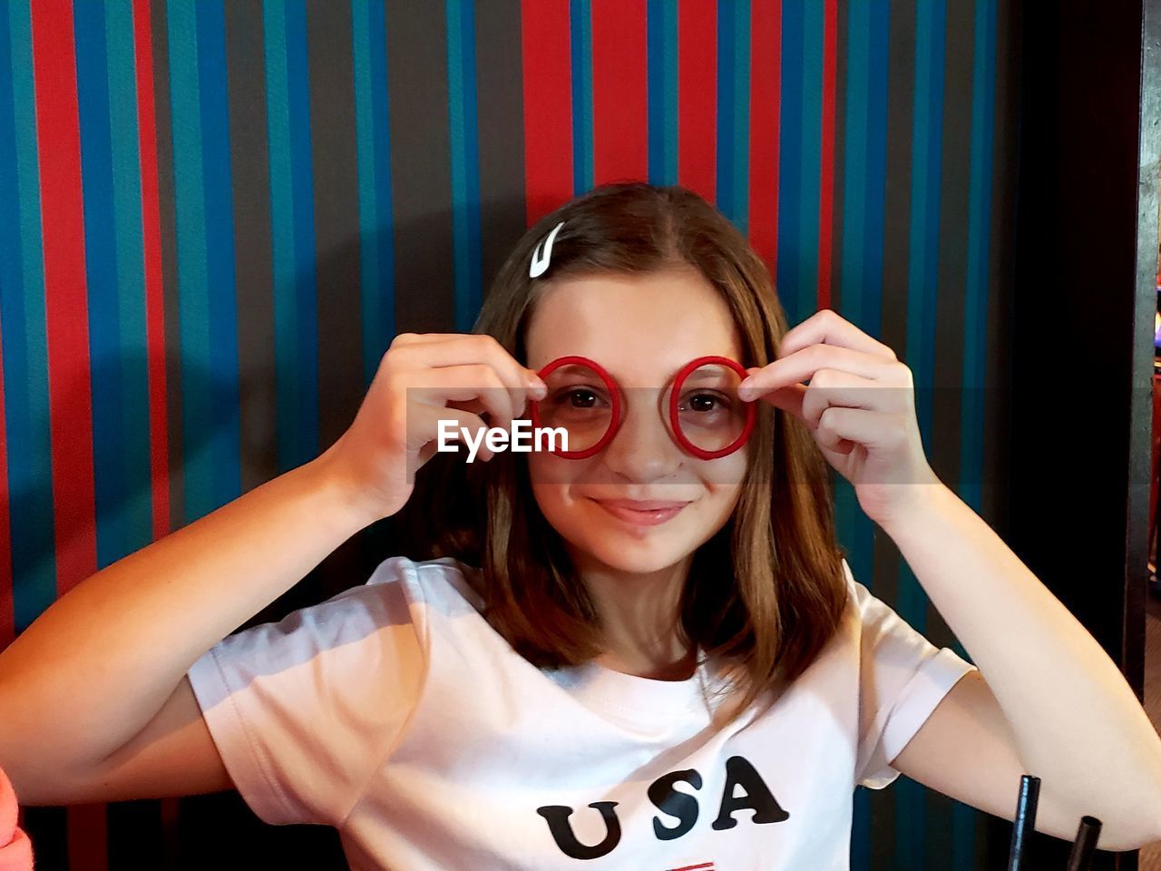 Portrait of girl holding rubber bands over eyes against wall