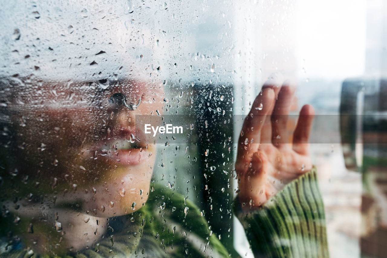 Melancholic young woman looking through window