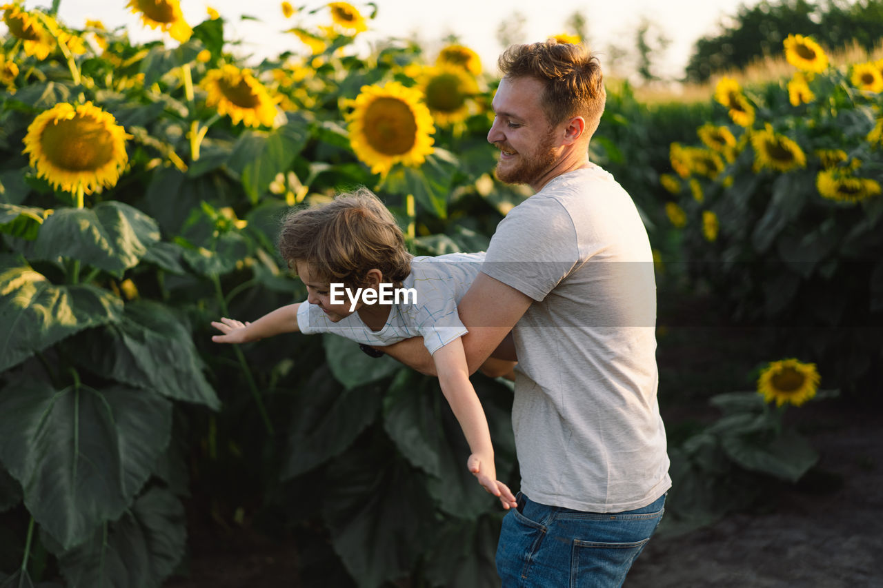 Father with little baby son in sunflowers field during golden hour. 